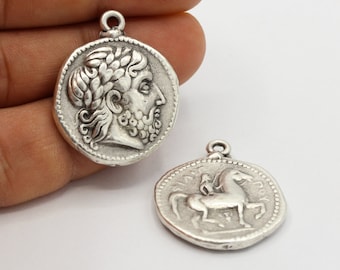May include: Two silver-toned metal pendants, one with a profile of a man with a laurel wreath and the other with a horse and rider.