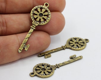 May include: Three antique gold-toned metal key charms with intricate floral designs. The keys have a textured surface and a loop at the top for attaching to jewelry or crafts.