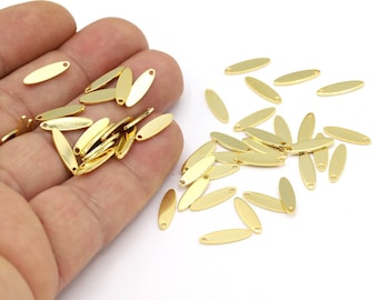May include: A pile of gold-colored metal oval-shaped charms with a hole in the center. The charms are scattered on a white surface.