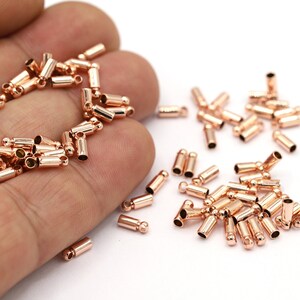 Peut inclure: Un grand nombre de embouts de bijoux en métal de couleur or rose. Les embouts sont cylindriques avec une petite boule à chaque extrémité.
