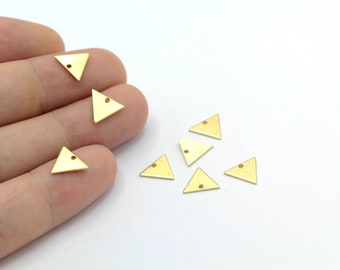 May include: A group of eight gold-colored triangle-shaped metal charms with a small hole at the top. The charms are scattered on a white surface.