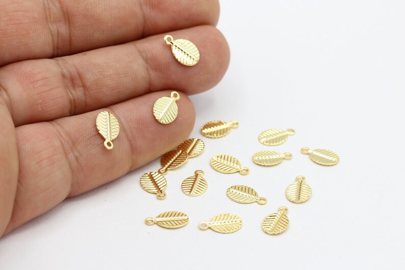 May include: A collection of gold leaf charms with a loop for attaching to jewelry or other crafts. The charms are scattered on a white surface.