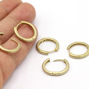 May include: Four gold hoop earrings with a hinged closure. The earrings are displayed on a hand.
