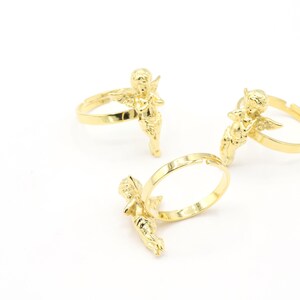 May include: Three gold-tone rings with angel figurines. Each ring features a detailed angel design with wings and a flowing gown.