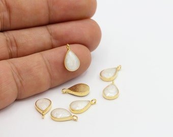 May include: A group of six gold-plated teardrop-shaped pendants with white pearlescent inlays. The pendants are arranged on a white surface.