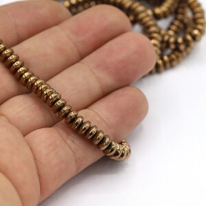 May include: A strand of gold-toned metal beads with a textured, hammered finish. The beads are round and have a slightly irregular shape.