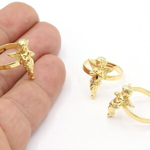 May include: Two gold-tone rings with an angel design. The angel is holding its hands together in a prayer position. The rings are adjustable.
