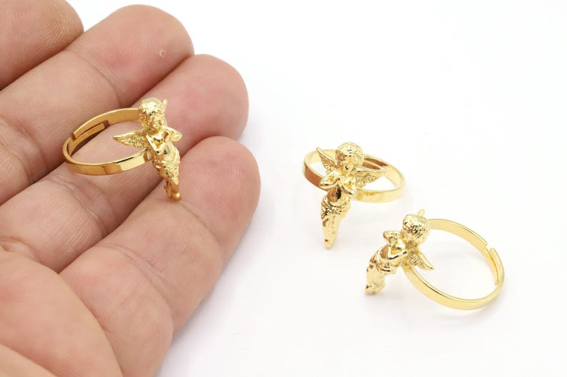 May include: Two gold-tone rings with an angel design. The angel is holding its hands together in a prayer position. The rings are adjustable.