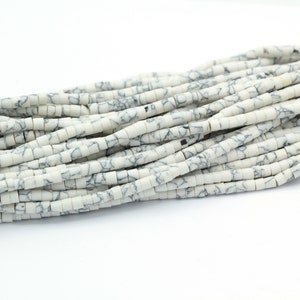 以下が含まれることがあります： 白と黒の大理石模様のビーズのストランド。ビーズは円筒形で、滑らかで磨かれた仕上げになっています。