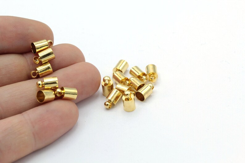 Puede incluir: Un grupo de tapones de extremo de metal dorado para la elaboraci&oacute;n de joyas. Los tapones tienen una peque&ntilde;a bola en un extremo y un agujero en el otro extremo.