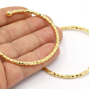 Può includere: Due braccialetti rigidi dorati con un motivo a diamante testurizzato e estremità arrotondate.