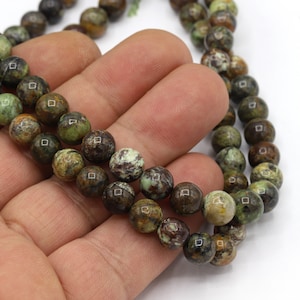 May include: Strands of round gemstone beads in shades of green, brown, and cream. The beads have a polished, glossy finish and are strung together. The beads are approximately 8mm in diameter.