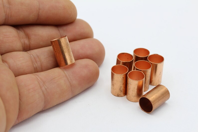 May include: A group of nine copper pipe fittings, some are stacked on top of each other, and one is being held in a hand.