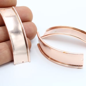 May include: Two rose gold metal curved strips with a smooth, polished finish. The strips are slightly curved and have a rounded edge.