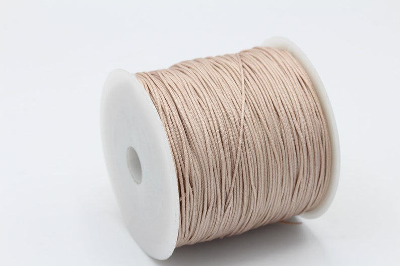 May include: A spool of beige waxed cord, a type of string used for jewelry making and crafts.