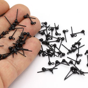 Könnte beinhalten: Nahaufnahme eines Stapels schwarzer Ohrring-Findings mit einer kleinen Kugel am Ende jedes Stiftes. Die Findings sind aus Metall und haben oben eine Öse zum Anbringen von Ohrringen.