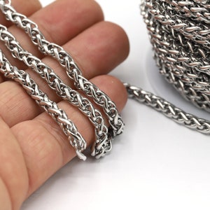 May include: A close-up of a silver braided chain. The chain is lying on a hand and a spool of the chain is in the background.