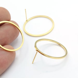May include: A pair of gold-toned hoop earrings with a simple, circular design. The earrings are made of metal and have a post closure.