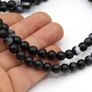 May include: A strand of black agate beads with white stripes. The beads are round and smooth, and they are strung on a clear cord.