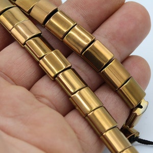 Peut inclure: Un bracelet en métal doré avec des maillons carrés. Le bracelet est composé de plusieurs pièces qui sont reliées entre elles.