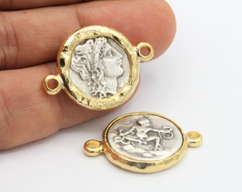 May include: Two gold-toned metal coin charms with a silver-toned design. One charm features a profile of a woman's face, the other features a figure holding a staff. Both charms have a loop on each side for attaching to a necklace or bracelet.