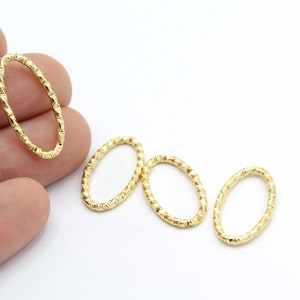 Puede incluir: Hallazgos de joyería ovalados dorados con una superficie texturizada. Los hallazgos se muestran sobre un fondo blanco. Una mano sostiene uno de los hallazgos. Estos hallazgos son adecuados para la fabricación de joyas.