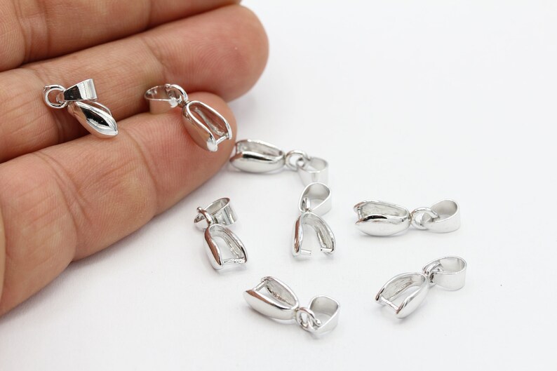 May include: Silver-toned metal pendant clasps, also known as bail clasps, for jewelry making. These clasps are designed to hold a pendant or charm securely.