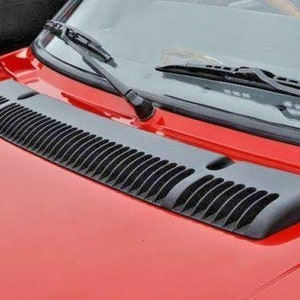 May include: A red car with a black plastic air vent on the hood.
