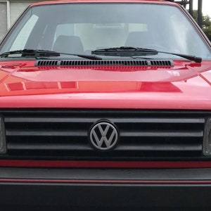 May include: A red Volkswagen Golf with a black grille and a silver Volkswagen logo. The car has a black bumper with a red stripe.