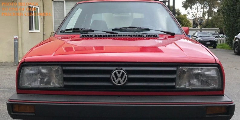May include: A red Volkswagen Golf with a black grille and a silver Volkswagen logo. The car has a black bumper with a red stripe.