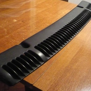 May include: Black plastic car windshield visor with a series of vertical vents. The visor is curved and has a smooth, glossy finish.