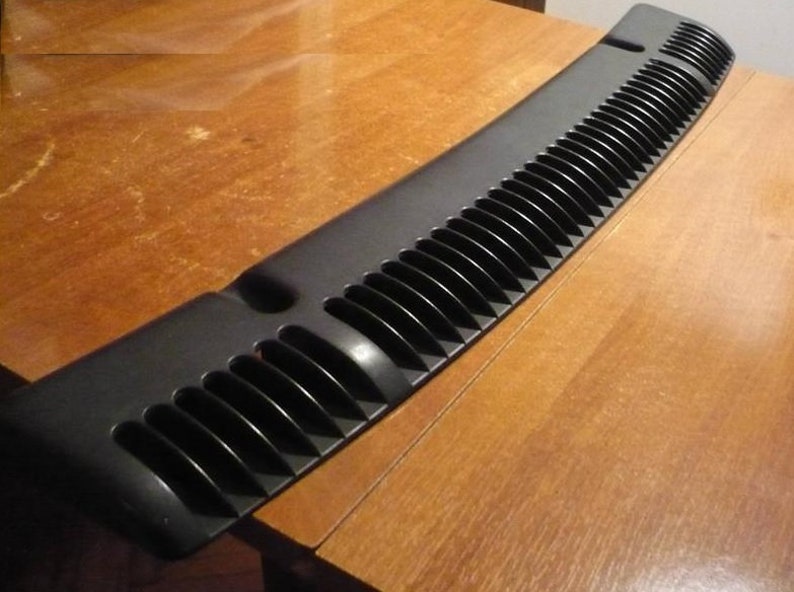 May include: Black plastic car windshield visor with a series of vertical vents. The visor is curved and has a smooth, glossy finish.
