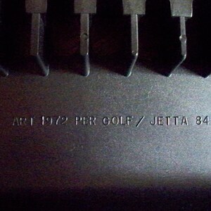 May include: Close-up of a black plastic part with the text "ART 1972 PER GOLF / JETTA 84 ->" printed on it.