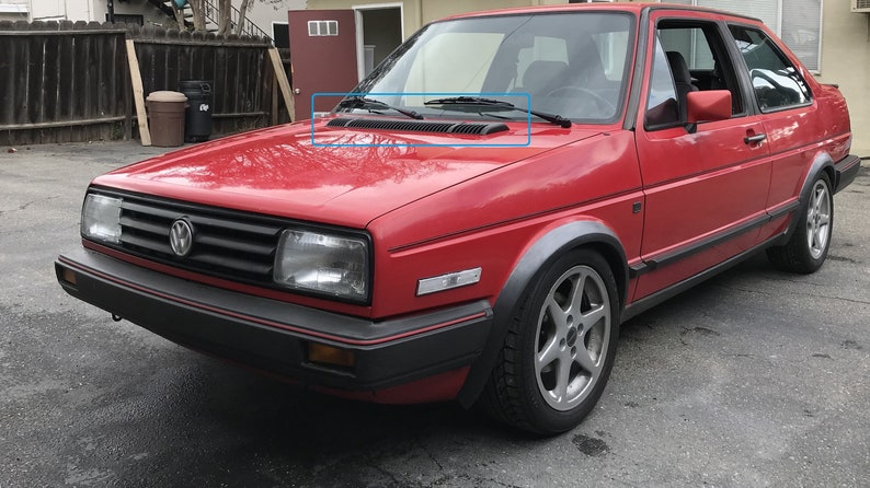 May include: A red Volkswagen Golf with black trim and a black grille. The car has a black windshield wiper and a black bumper.