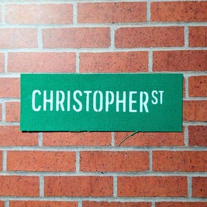 Könnte beinhalten: Ein grünes Straßenschild mit weißem Text, auf dem "CHRISTOPHER ST." steht.