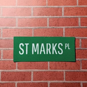 May include: A green street sign with white text that reads "ST MARKS PL".