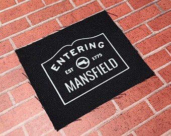 May include: Black fabric patch with white text that reads "Entering Est. 1775 Mansfield" with a circle containing a stylized map of the state of Connecticut.