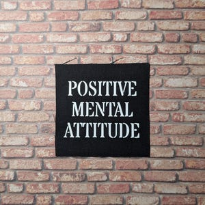 May include: Black fabric patch with white text that reads "POSITIVE MENTAL ATTITUDE".