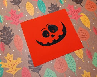 May include: A red fabric patch with a black silhouette of a smiling jack-o'-lantern face.