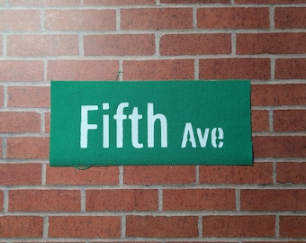 May include: A green street sign with white text that reads "Fifth Ave".