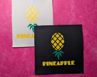 May include: Two fabric patches with a pineapple design. The first patch is white with a gold pineapple and the text "PINEA" in yellow. The second patch is black with a yellow pineapple and the text "PINEAPPLE" in yellow.