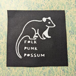 Puede incluir: Parche de tela negro con un contorno blanco de un opossum y el texto "Folk Punk Possum".