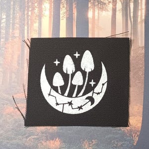 May include: Black fabric patch with a white crescent moon and four white mushrooms with stars. The mushrooms are clustered together in the center of the moon.