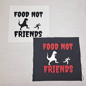 Puede incluir: Dos parches en blanco y negro con el texto "Food Not Friends" y una silueta de un dinosaurio y una persona corriendo. Los parches están sobre un fondo a cuadros blanco y negro.