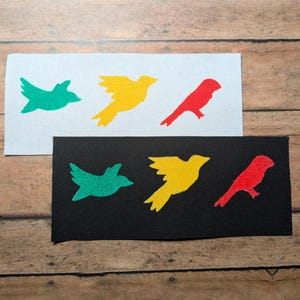 May include: Two fabric panels with a black and white background. Each panel features three bird silhouettes in different colors: green, yellow, and red.