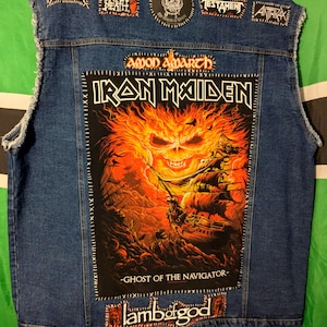 May include: A blue denim vest with various band patches, including Iron Maiden, Amon Amarth, Lamb of God, Megadeth, Testament, Anthrax, and Watershed. The Iron Maiden patch features a skull engulfed in flames and the text "Ghost of the Navigator".