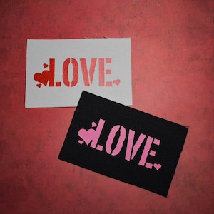 Può includere: Due toppe di tessuto con la parola "LOVE" stampata in lettere rosse e rosa. Le toppe sono su uno sfondo rosso.