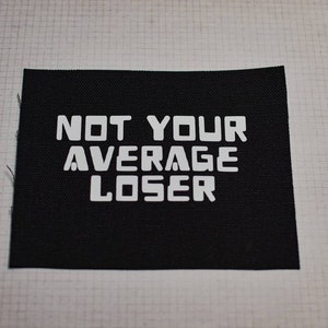May include: Black fabric patch with white text that reads "NOT YOUR AVERAGE LOSER".