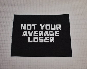 May include: Black fabric patch with white text that reads "NOT YOUR AVERAGE LOSER".