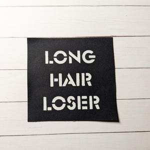 May include: Black fabric patch with white text that reads "LONG HAIR LOSER".